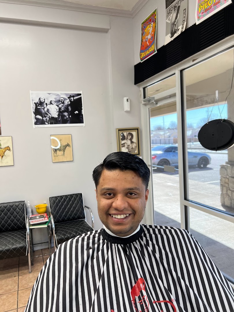 Inside Gills — a smiling client in the striped cape, a black-and-white class photo of older barbers on the wall, US storefront windows beyond.
