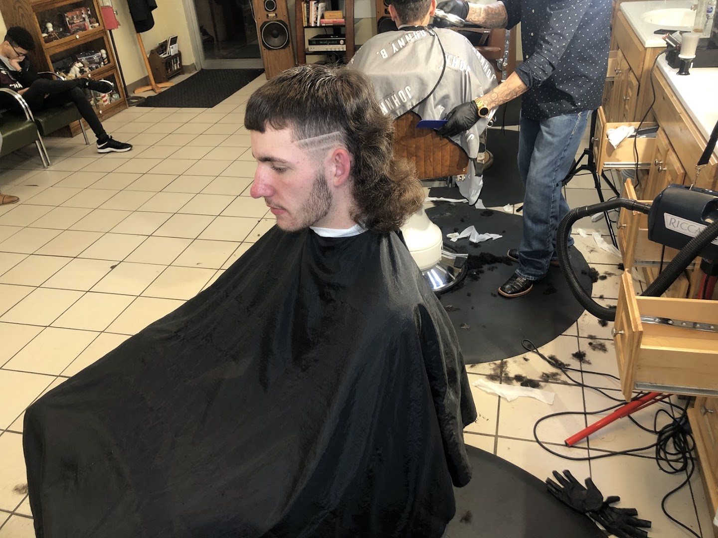 A finished pompadour-fade cut at Gills — striped cape, mirror behind, Tulsa storefront windows visible.