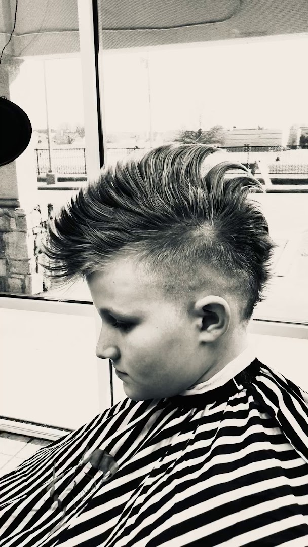A finished pompadour cut at Gills — Tulsa storefront windows behind, black-and-white treatment, a younger client in a striped cape.