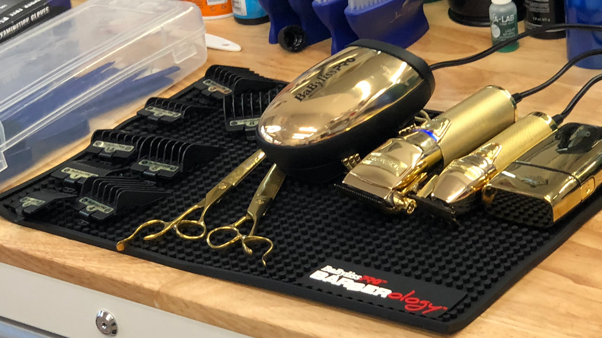 Gold-plated BabylissPro clippers, trimmers and shears arranged on a black barber mat at Gills.